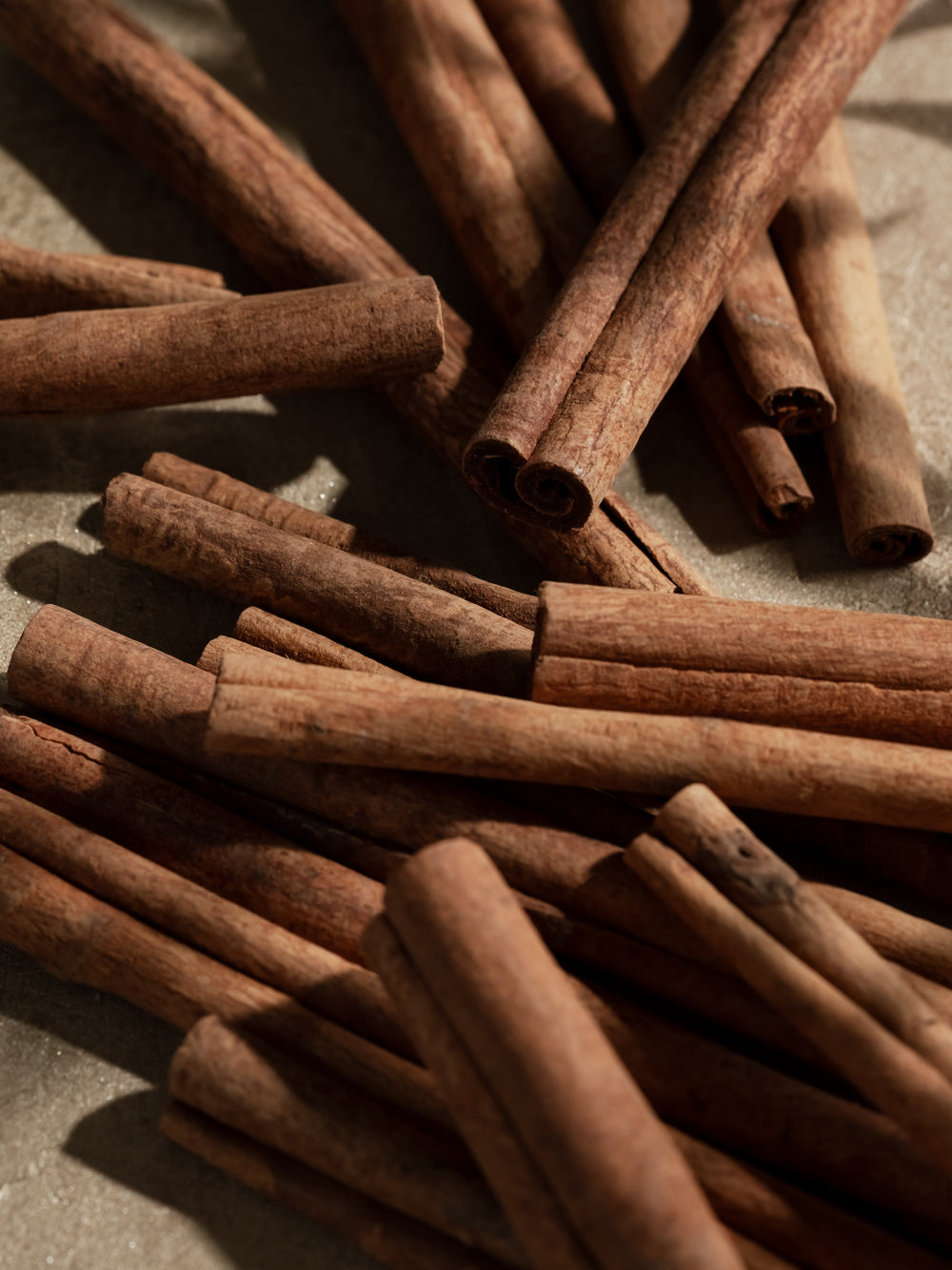 Close-up of scattered cinnamon sticks on a gray surface, ingredient photo for Pura Cinnamon Cider.