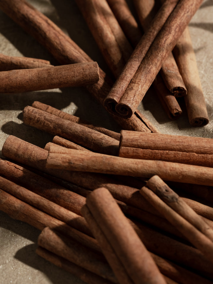 Close-up of scattered cinnamon sticks on a gray surface, ingredient photo for Pura Cinnamon Cider.