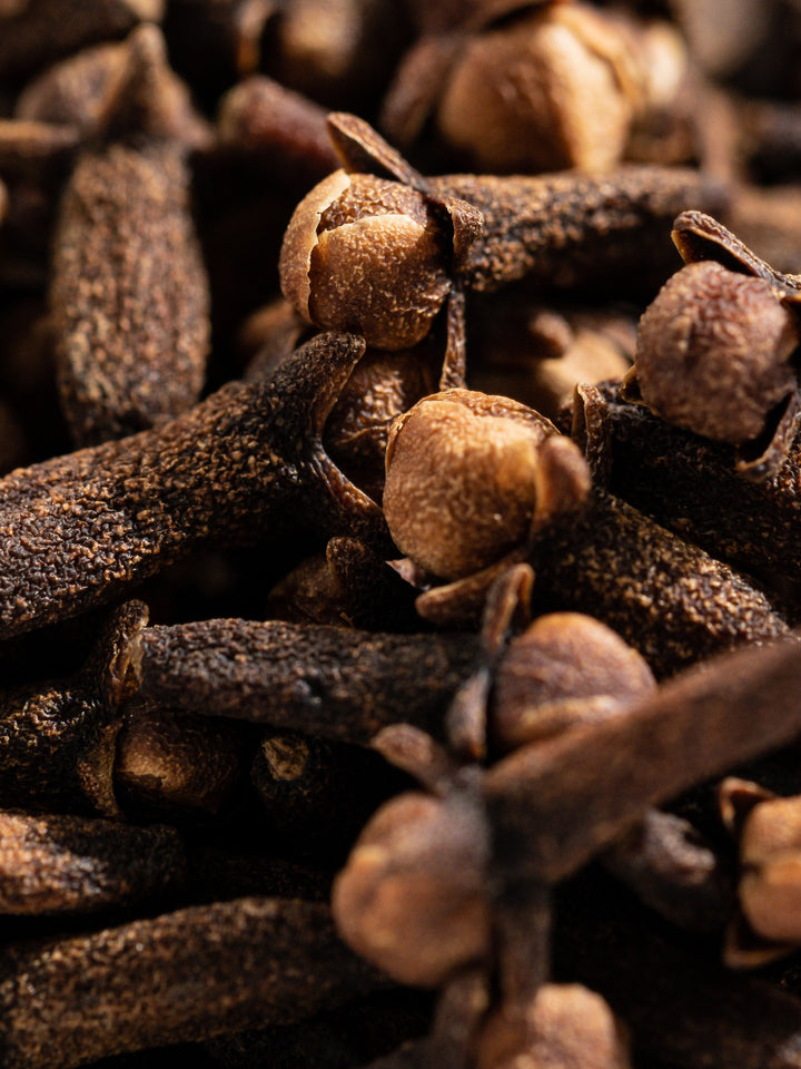 Close-up macro shot of whole dried cloves, a key ingredient in Pura Pumpkin Spice fragrance vial.