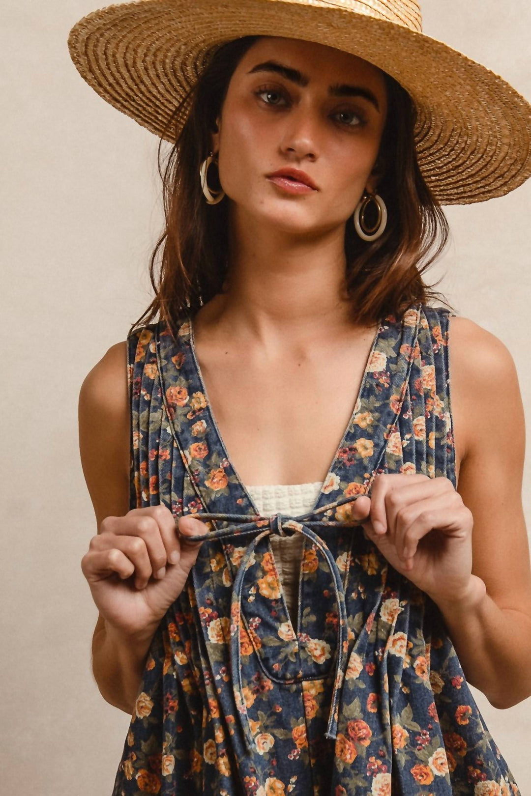 Woman wearing denim blue floral romper with tie waist and straw hat