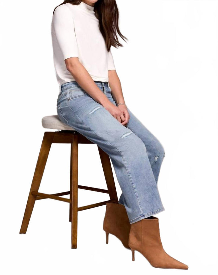 Woman wearing light blue straight leg flood jeans with white top and brown boots