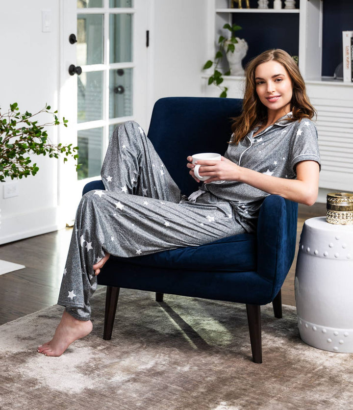 Woman wearing gray star-print pajama set relaxing in navy chair with coffee cup