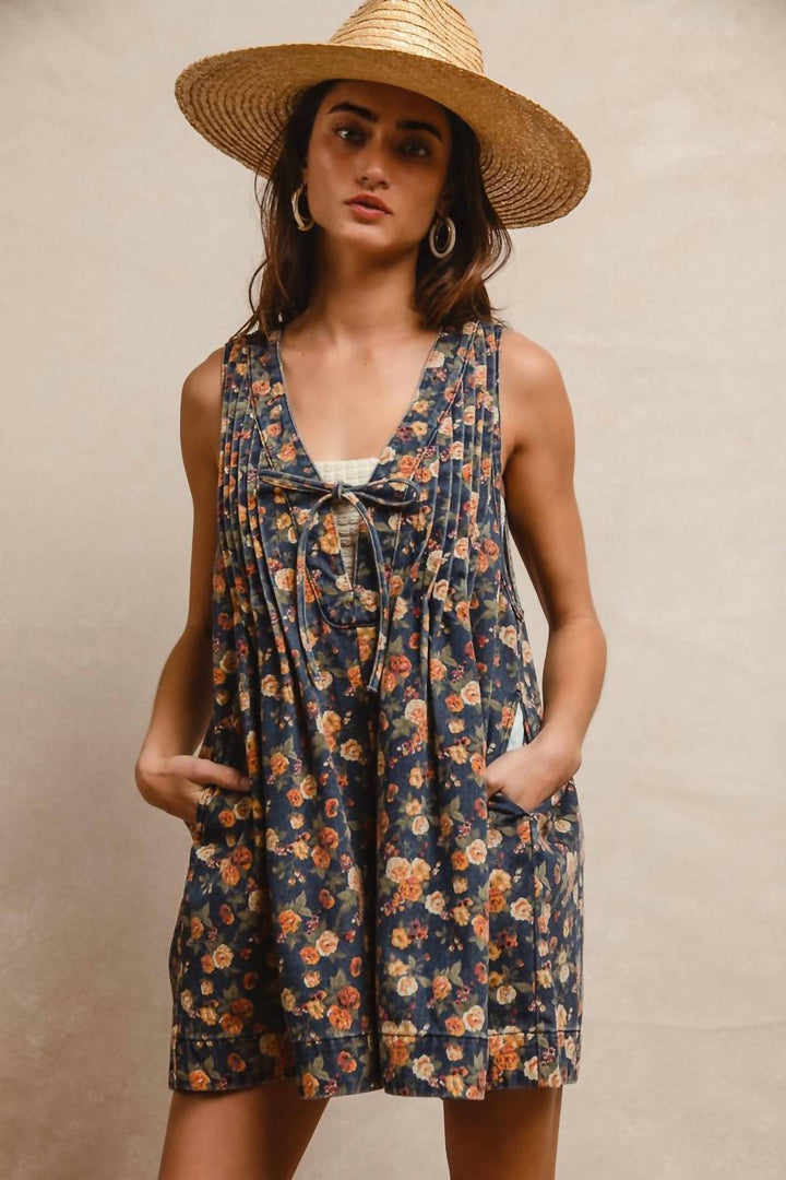 Woman wearing navy floral denim romper with tie detail and straw hat