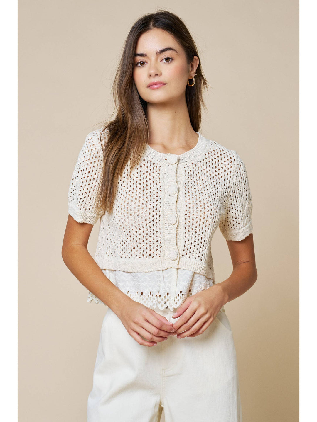 Woman wearing cream open-knit short sleeve cardigan with lace trim and white pants