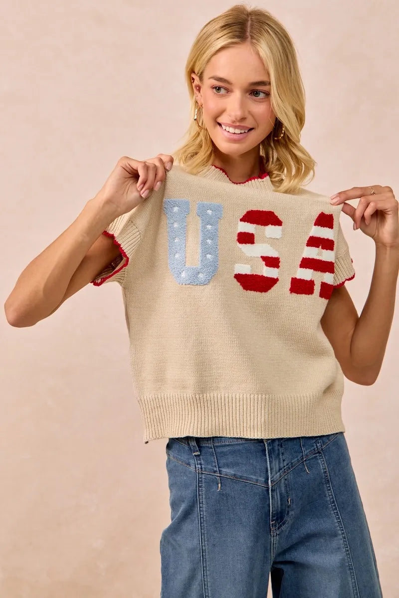 Woman wearing oatmeal knit sweater vest with USA patchwork lettering in blue and red