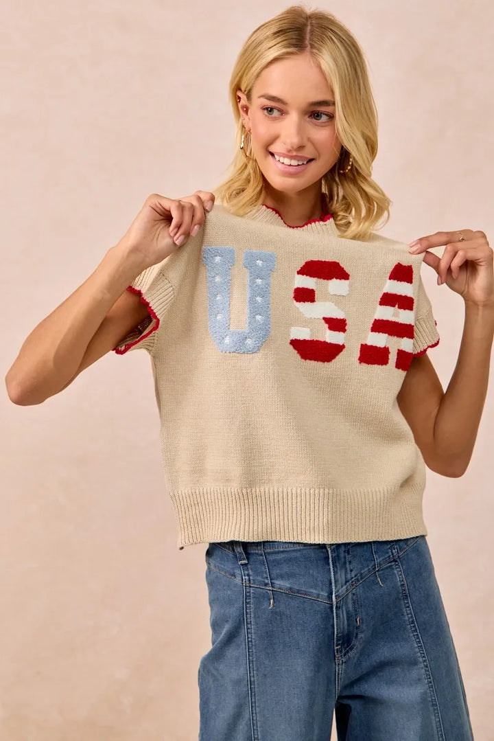 Woman wearing oatmeal knit sweater vest with USA patchwork lettering in blue and red
