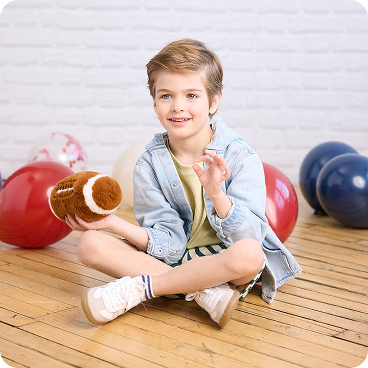 Child holding brown Warmies football plush toy with white laces and stitching