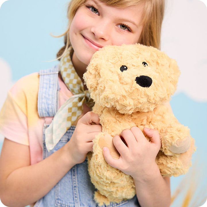 Young girl holding golden plush Warmies stuffed dog toy with soft curly fur