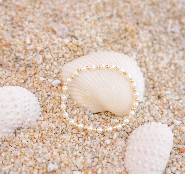 Beaded Blondes Luci Pearl Bracelet in gold displayed on a seashell in sand