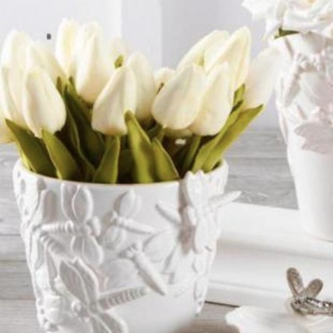White artificial tulip stems arranged in decorative white textured vase on white surface