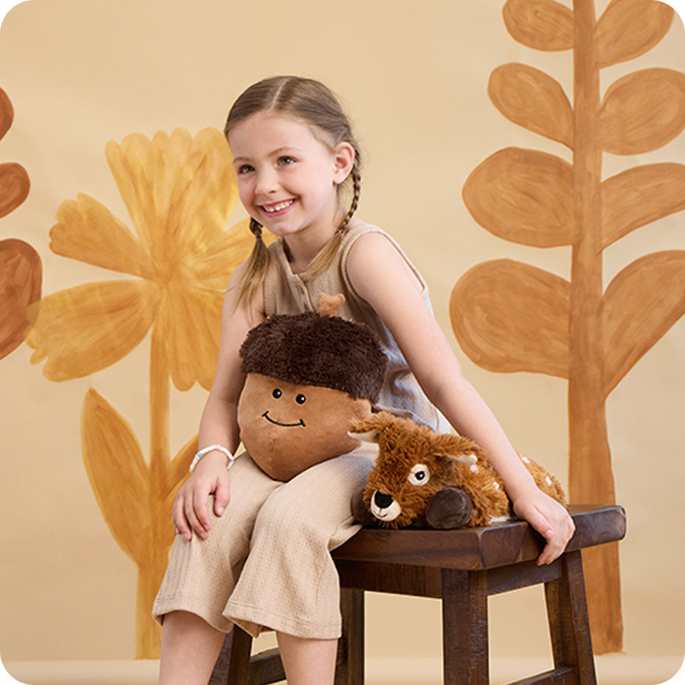 Child holding brown Warmies laying deer plush toy with acorn pillow