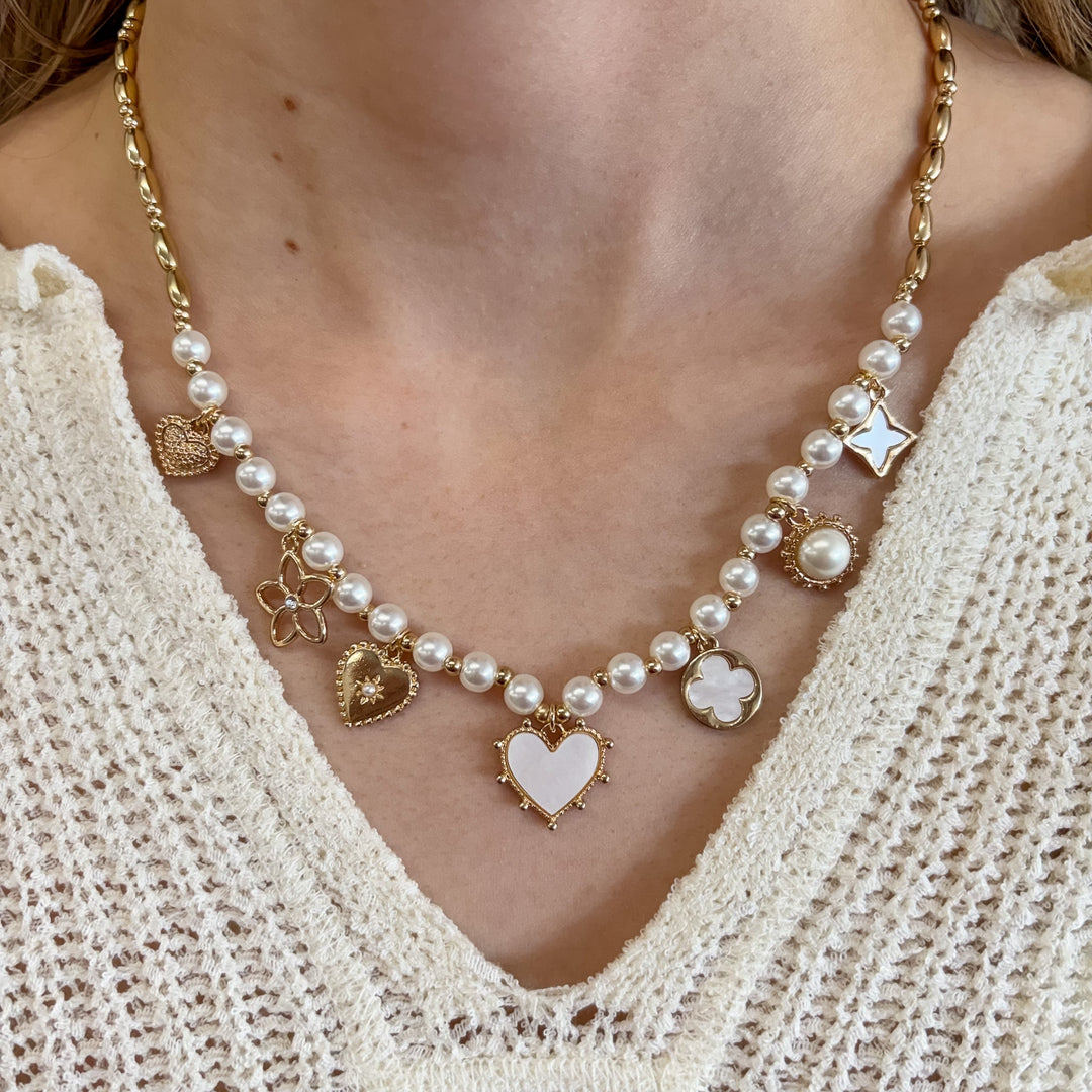 Gold chain necklace with white pearls and mixed charm pendants including hearts, flowers, and stars
