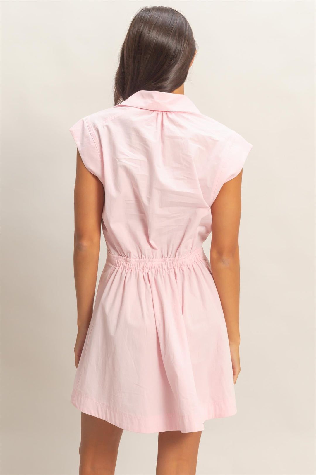 Woman wearing soft pink sleeveless collared shirred mini dress from behind
