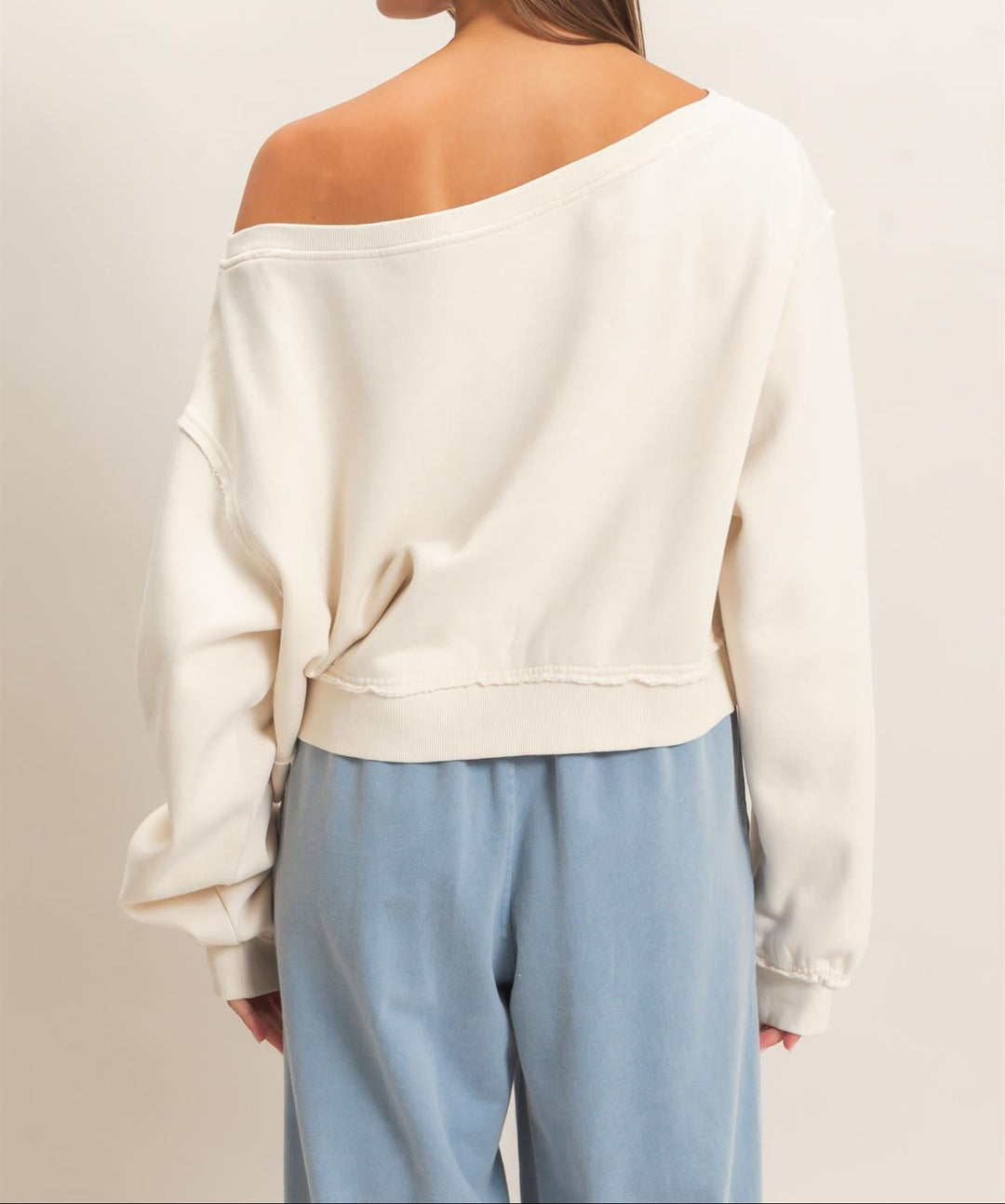 Back view of off-shoulder cream sweatshirt with raw edge hem detail on model
