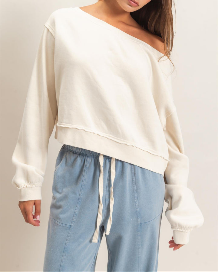 HYFVE Raw Edge Off the Shoulder Sweatshirt in Alpaca cream color, paired with blue joggers