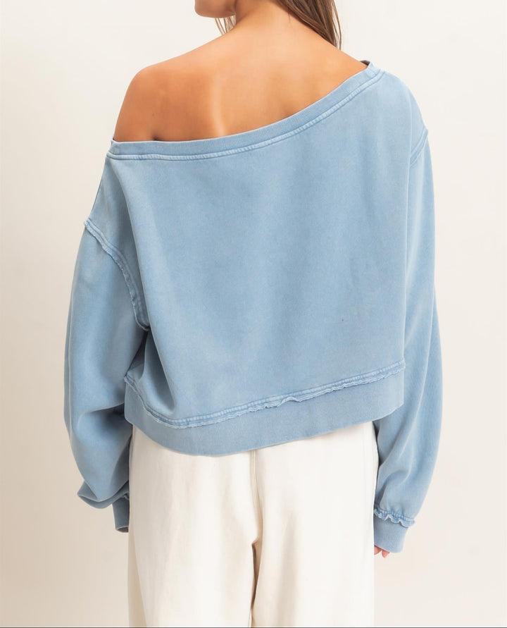 Back view of HYFVE Raw Edge Off the Shoulder Sweatshirt in dusty blue, styled with white pants.