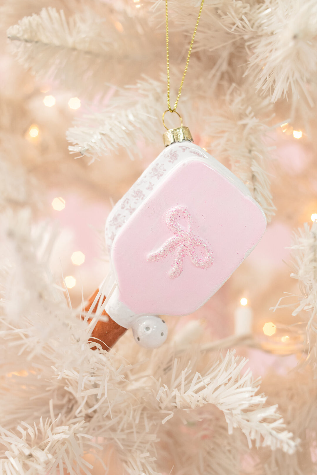 Pink pickleball paddle Christmas ornament with glitter bow hanging on white tree