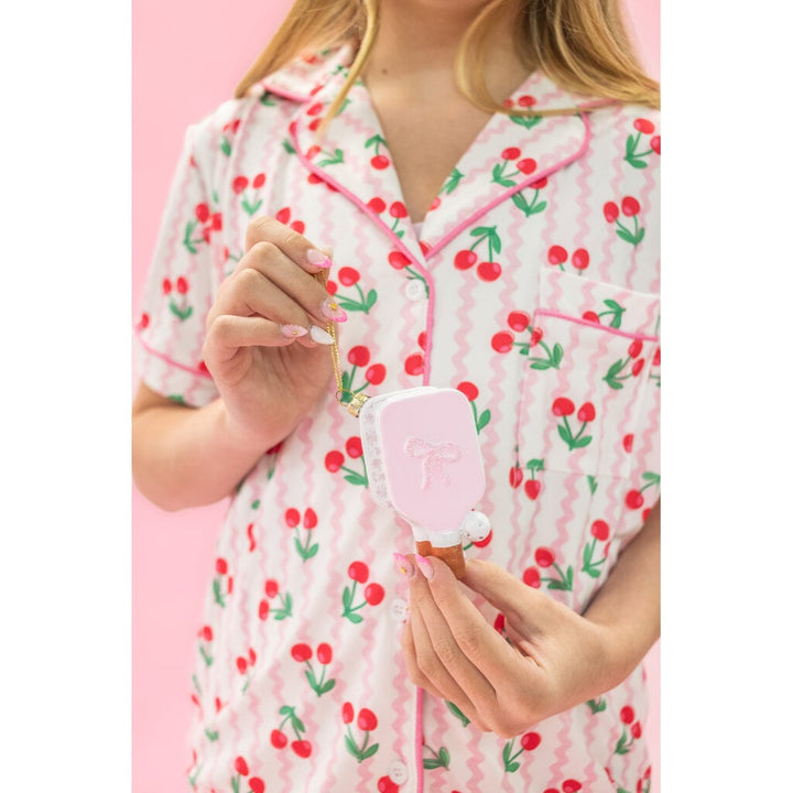 Hand holding a pink pickleball paddle-shaped Christmas ornament with bow detail and gold chain