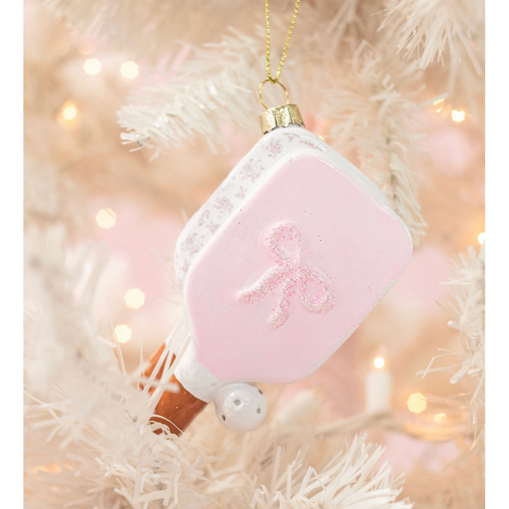 Pink pickleball paddle Christmas ornament with glitter bow hanging on white tree
