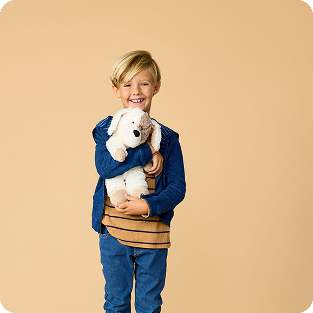 Child holding white and cream Warmies puppy plush toy with floppy ears