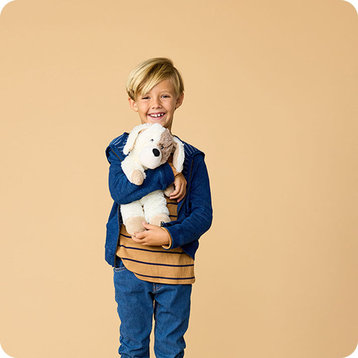 Child holding white and cream Warmies puppy plush toy with floppy ears