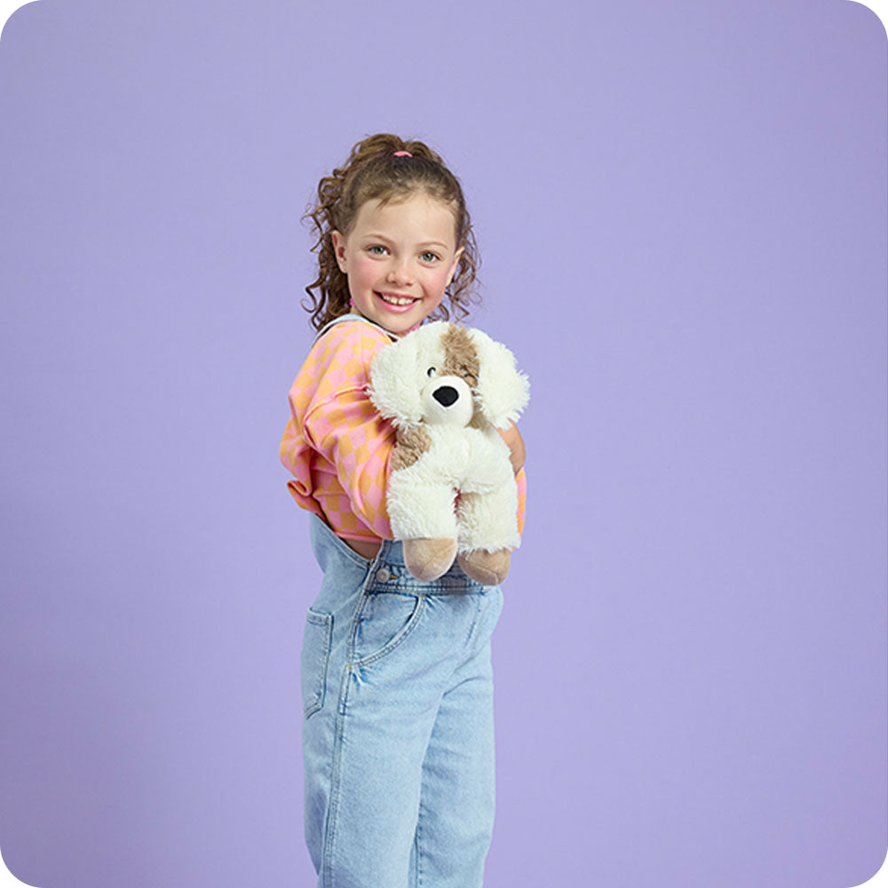 Child holding Warmies cream and brown plush puppy stuffed animal toy