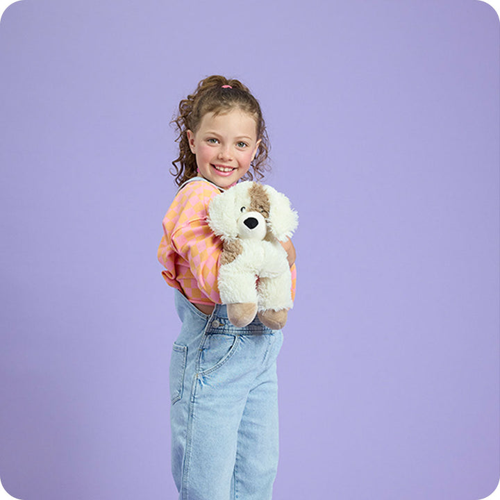 Child holding Warmies cream and brown plush puppy stuffed animal toy