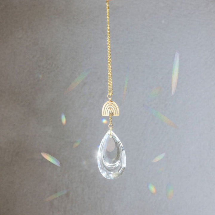 Clear crystal teardrop suncatcher with gold rainbow charm creating prismatic light effects