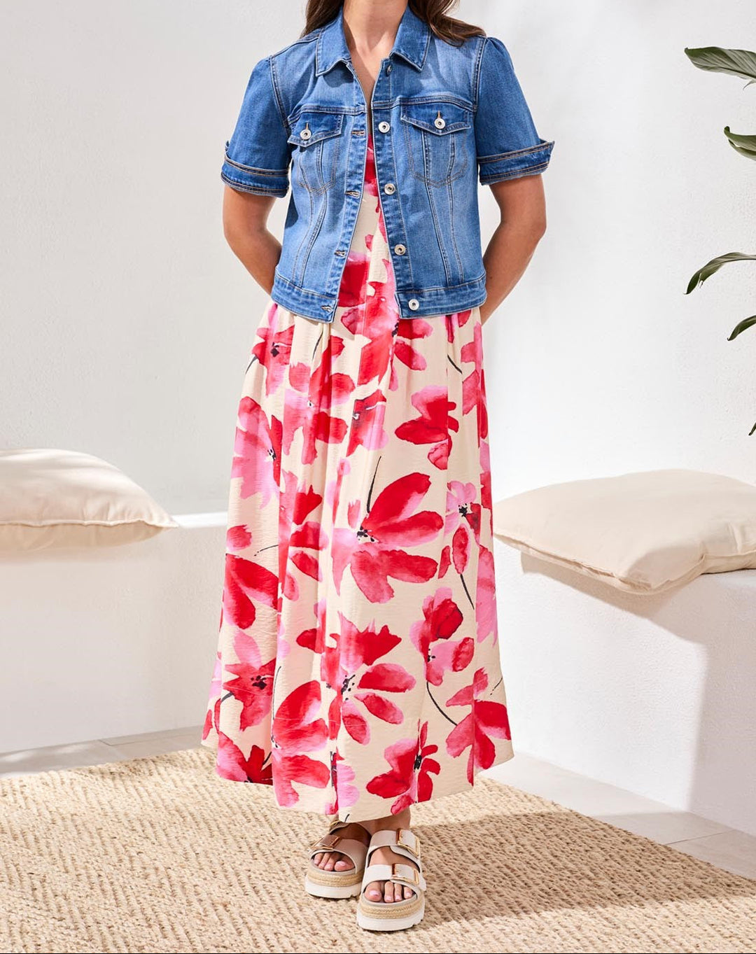 Woman wearing blue denim elbow sleeve jacket over floral dress in studio setting