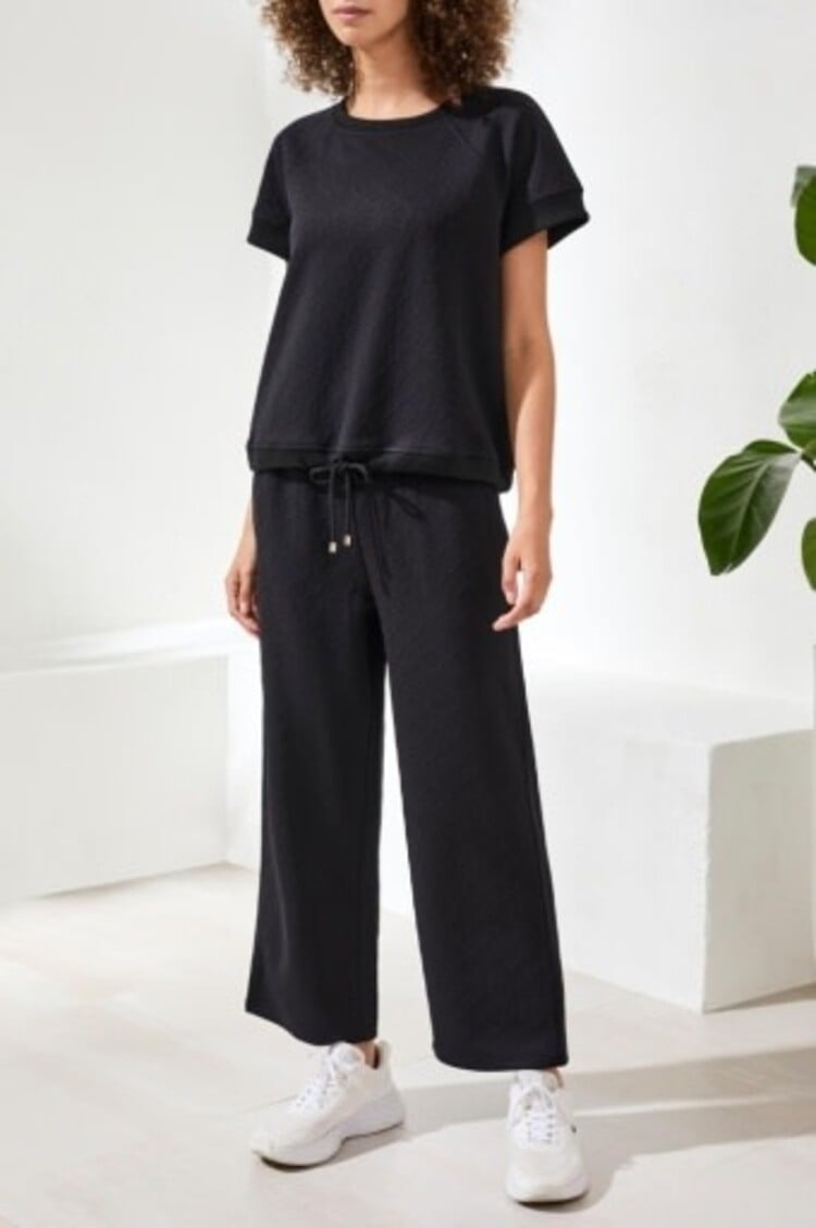 Woman wearing black crew neck top with matching drawstring wide-leg pants and white sneakers