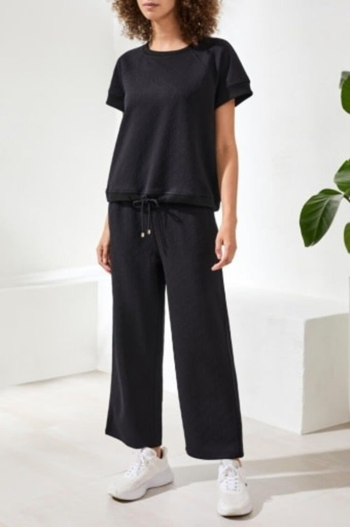 Woman wearing black crew neck top with matching drawstring wide-leg pants and white sneakers