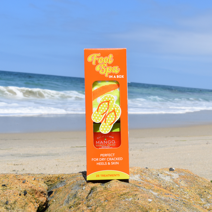 California Mango Foot Spa in a Box kit displayed on a beach rock with ocean background